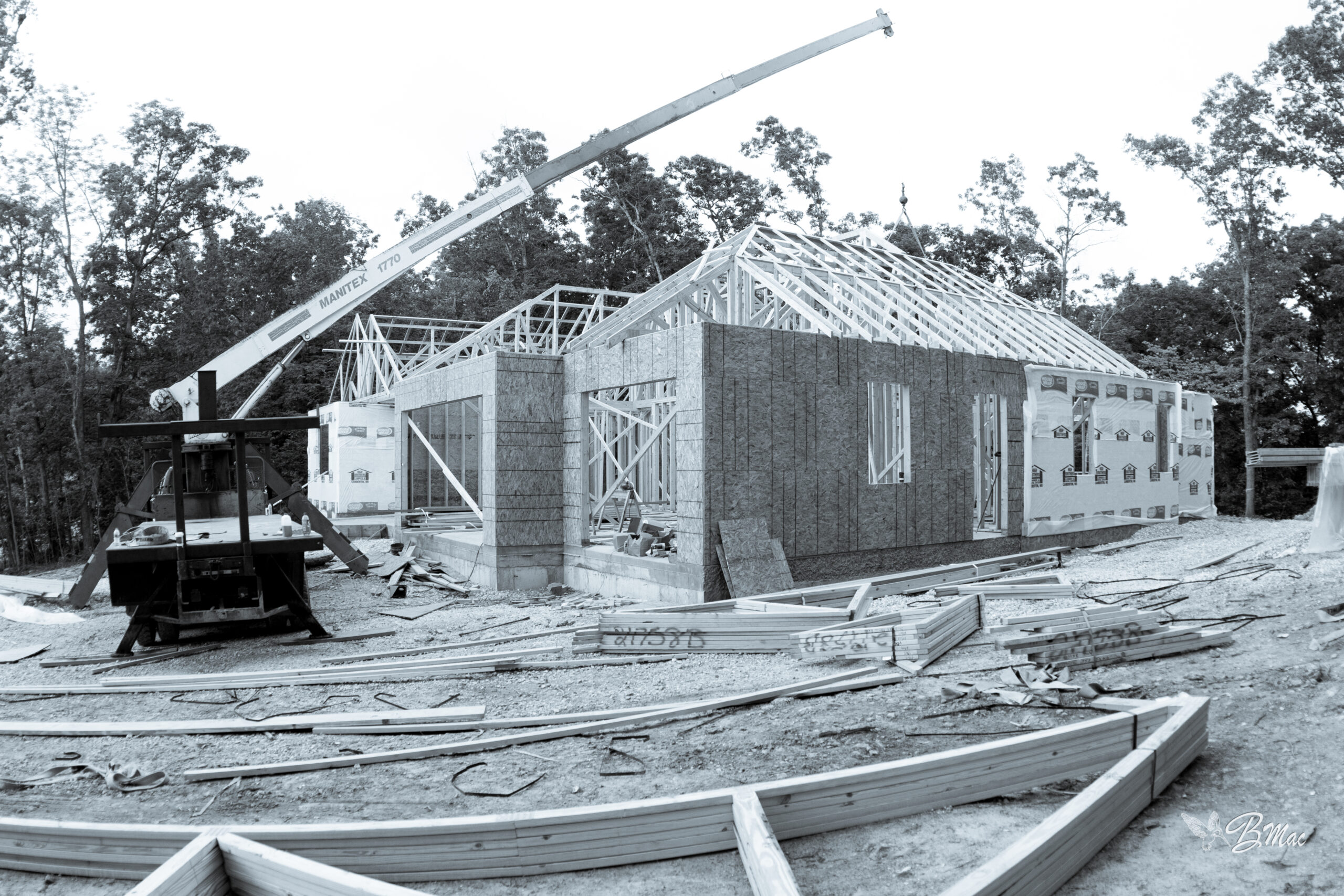 Black-and-white photograph of a MANITEX 1770 crane setting roof trusses on a Cloke Custom Homes mid-build at the Lake of the Ozarks