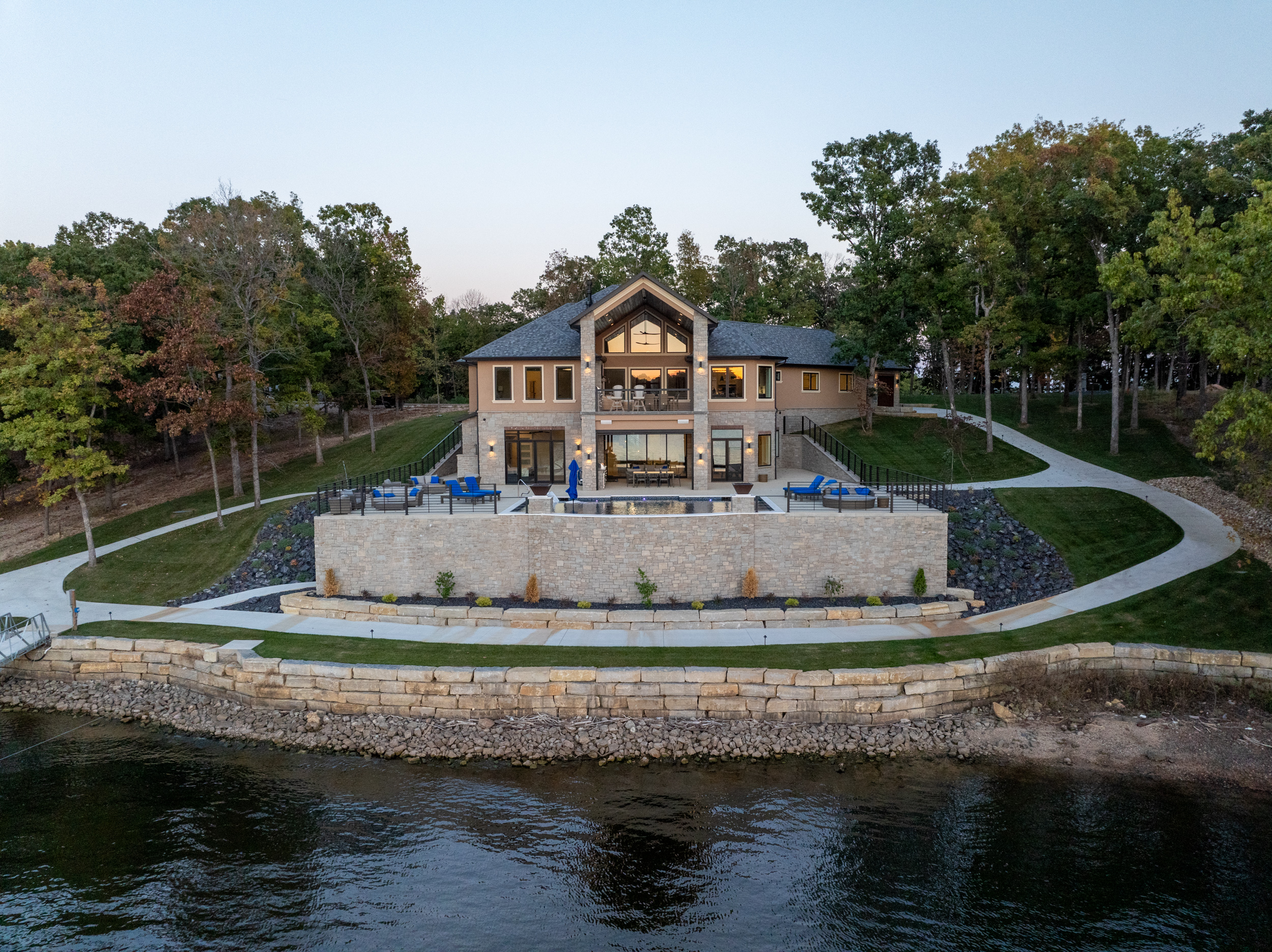 Cloke Custom Homes lakefront stone home at dusk with infinity pool, cove view