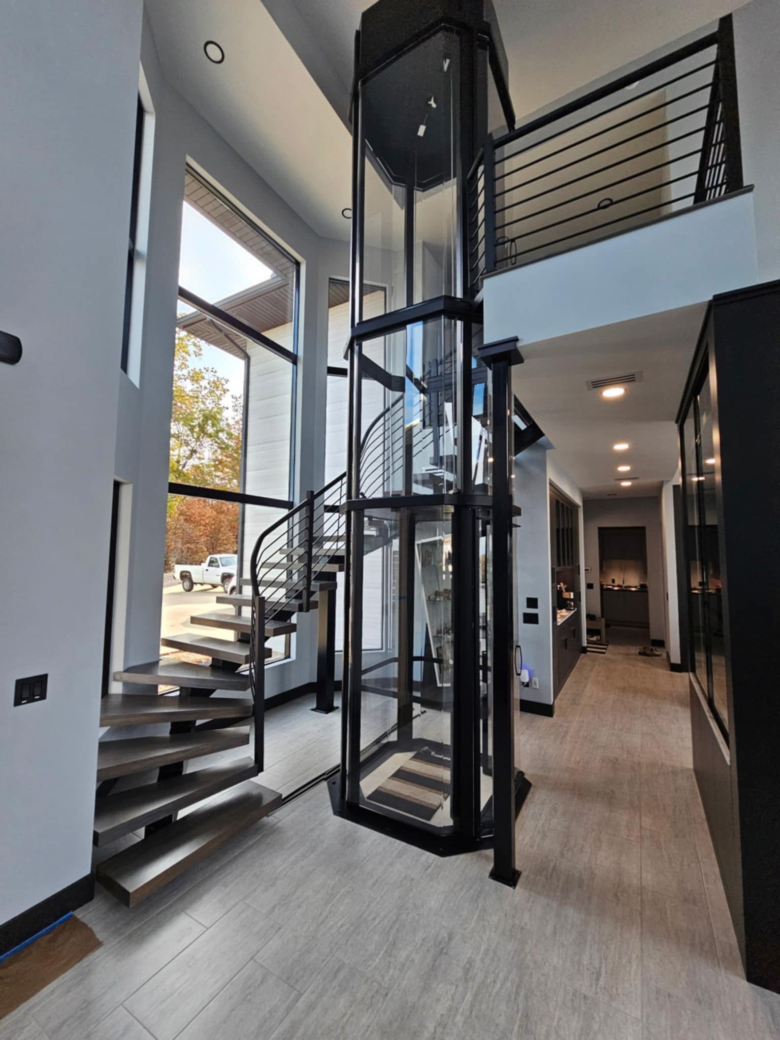 Custom floating staircase wrapping a glass elevator shaft by Cloke Custom Homes