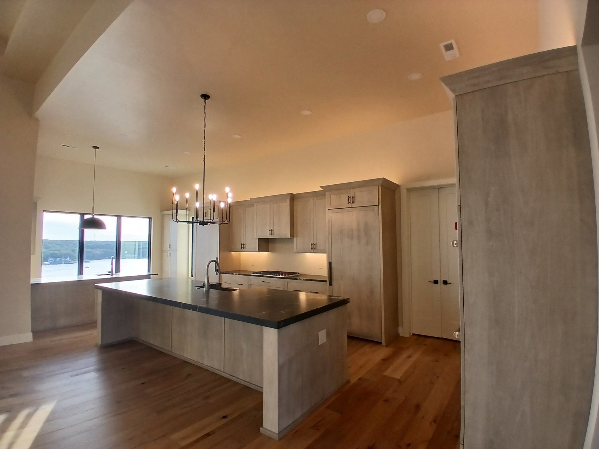 Modern kitchen island and dining with lake views by Cloke Custom Homes